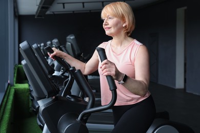 Photo of Senior woman training on elliptical machine in gym