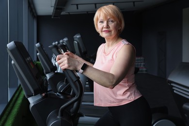 Photo of Senior woman training on elliptical machine in gym