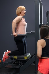 Photo of Senior woman training on power tower supervised by professional trainer in gym