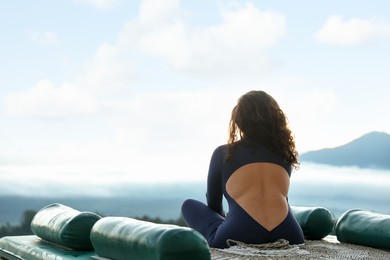 Photo of Woman meditating on mat in mountains, back view. Space for text