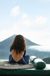 Photo of Woman meditating on mat in mountains, back view. Space for text