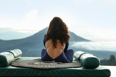 Photo of Woman meditating on mat in mountains, back view