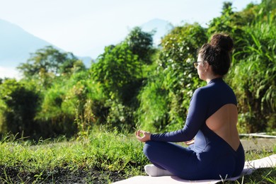 Photo of Woman meditating on yoga mat outdoors. Space for text