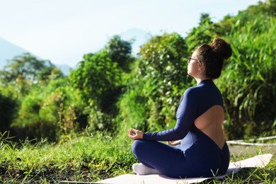 Photo of Woman meditating on yoga mat outdoors. Space for text