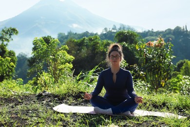 Photo of Woman meditating on yoga mat outdoors. Space for text