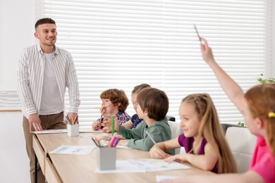 Photo of Man teaching kids to draw at painting lesson indoors