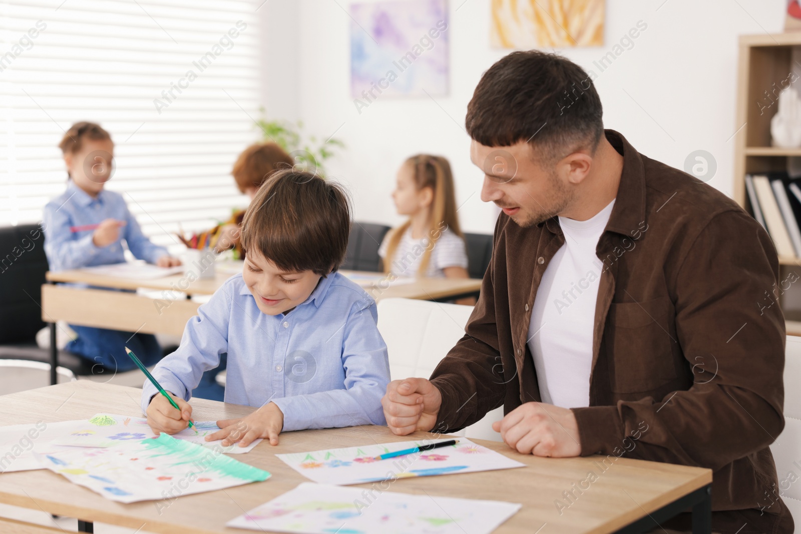 Man teaching kid to draw at painting lesson indoors, selective focus Photo of Man teaching kid to draw at painting lesson indoors, selective focus
