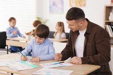 Photo of Man teaching kid to draw at painting lesson indoors, selective focus