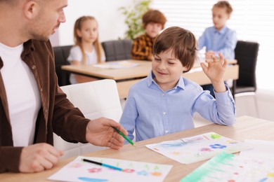 Photo of Man teaching kid to draw at painting lesson indoors, selective focus