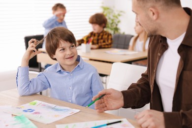Photo of Man teaching kid to draw at painting lesson indoors, selective focus