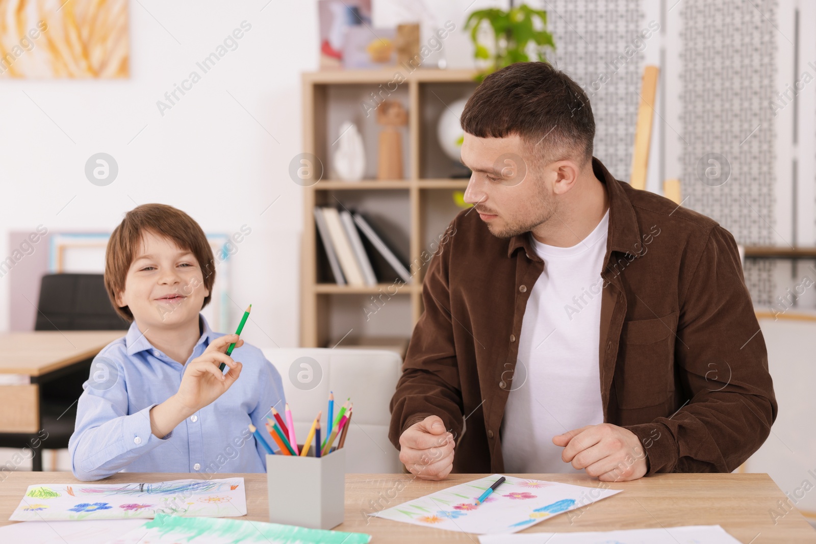 Man teaching kid to draw at painting lesson indoors Photo of Man teaching kid to draw at painting lesson indoors