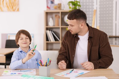 Photo of Man teaching kid to draw at painting lesson indoors