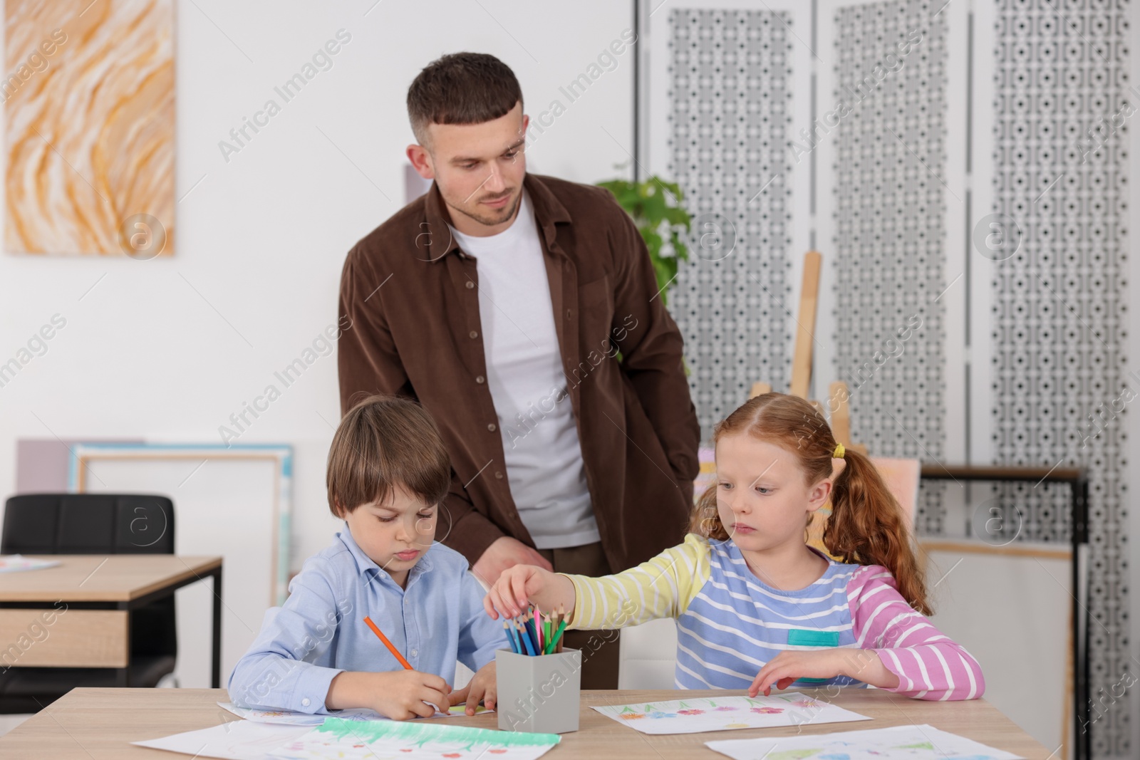 Man teaching kids to draw at painting lesson indoors Photo of Man teaching kids to draw at painting lesson indoors