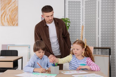 Photo of Man teaching kids to draw at painting lesson indoors