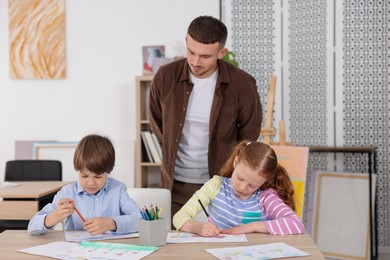 Photo of Man teaching kids to draw at painting lesson indoors