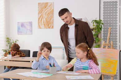 Photo of Man teaching kids to draw at painting lesson indoors