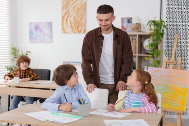 Photo of Man teaching kids to draw at painting lesson indoors