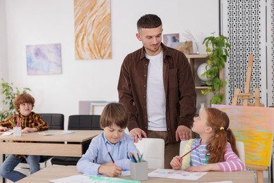Photo of Man teaching kids to draw at painting lesson indoors