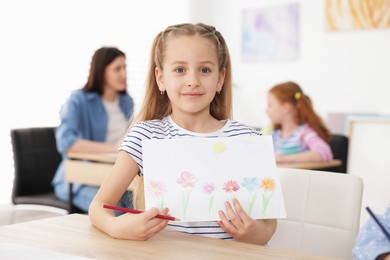 Photo of Cute girl showing her drawing during painting lesson indoors, selective focus