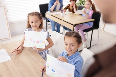 Photo of Kids showing their drawings to teacher at painting lesson indoors, selective focus