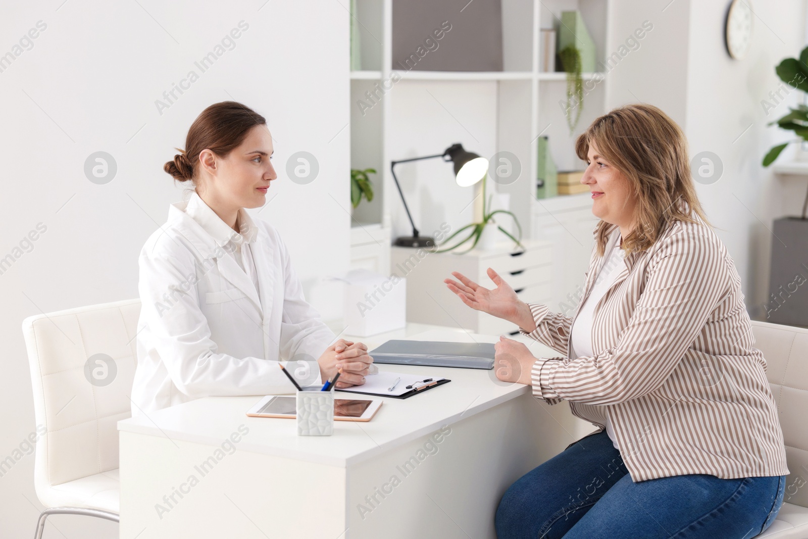 Photo of Weight loss. Nutritionist consulting overweight woman at white desk in clinic