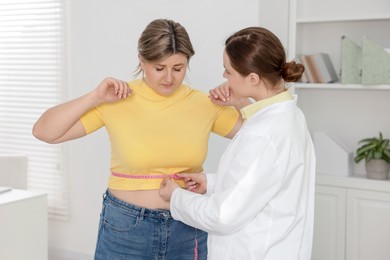 Photo of Weight loss. Nutritionist measuring overweight woman's waist with tape in clinic
