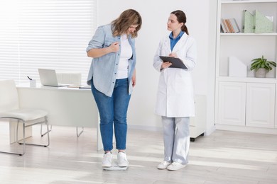 Photo of Weight loss. Overweight woman standing on scales during consultation with nutritionist in clinic