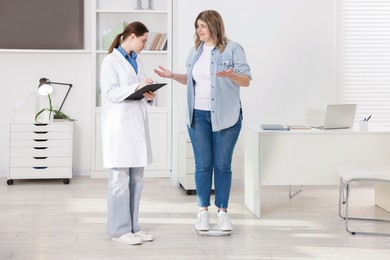 Photo of Weight loss. Overweight woman standing on scales during consultation with nutritionist in clinic