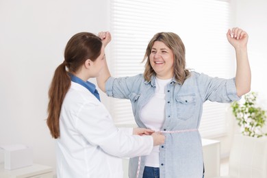 Photo of Weight loss. Nutritionist measuring happy overweight woman's waist with tape in clinic