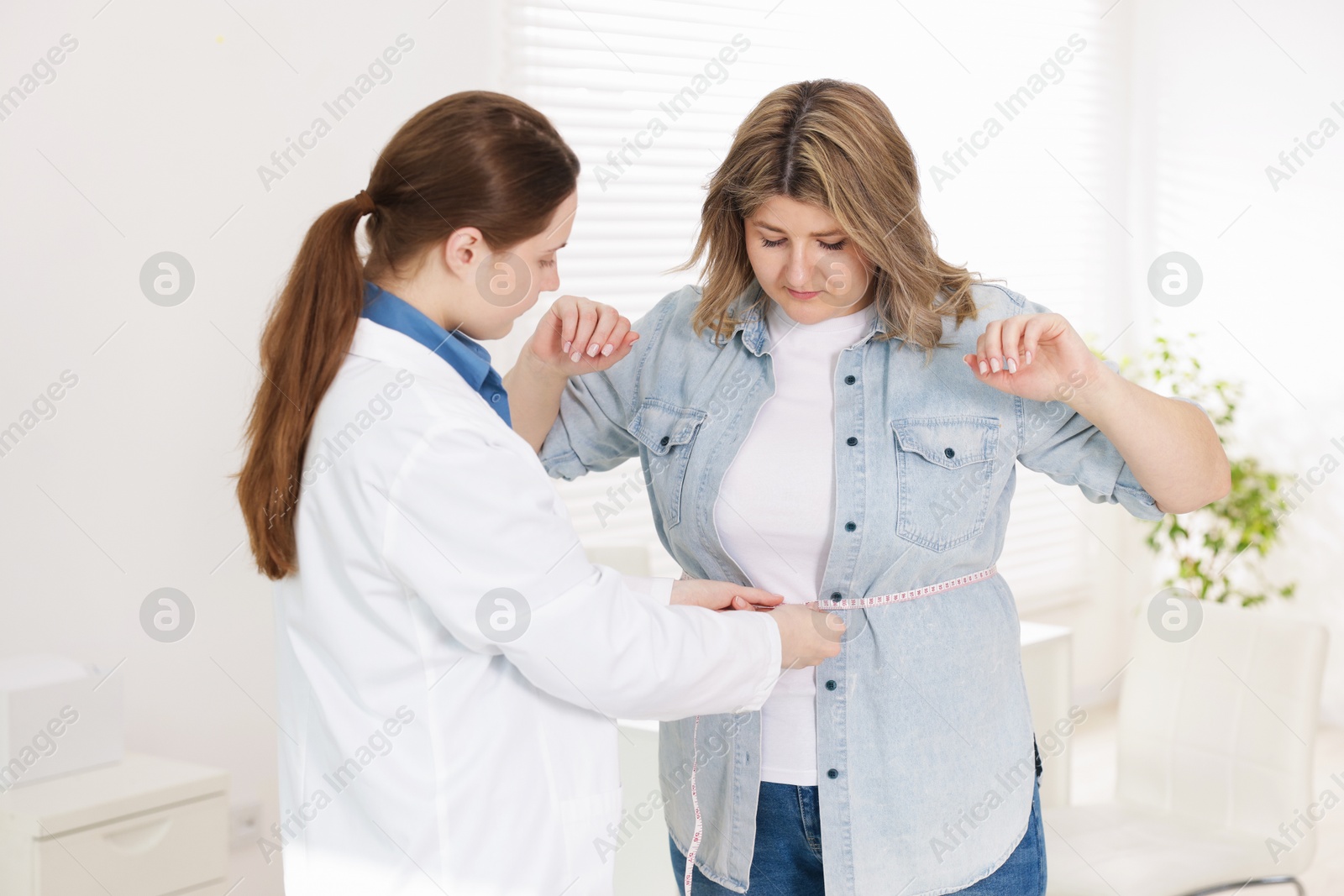 Photo of Weight loss. Nutritionist measuring overweight woman's waist with tape in clinic