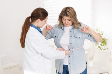 Photo of Weight loss. Nutritionist measuring overweight woman's waist with tape in clinic