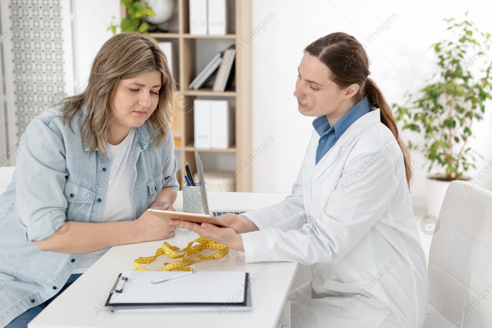 Photo of Weight loss. Nutritionist consulting overweight woman at white desk in clinic