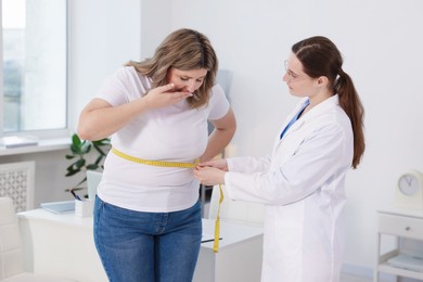 Photo of Weight loss. Nutritionist measuring shocked overweight woman's waist with tape in clinic