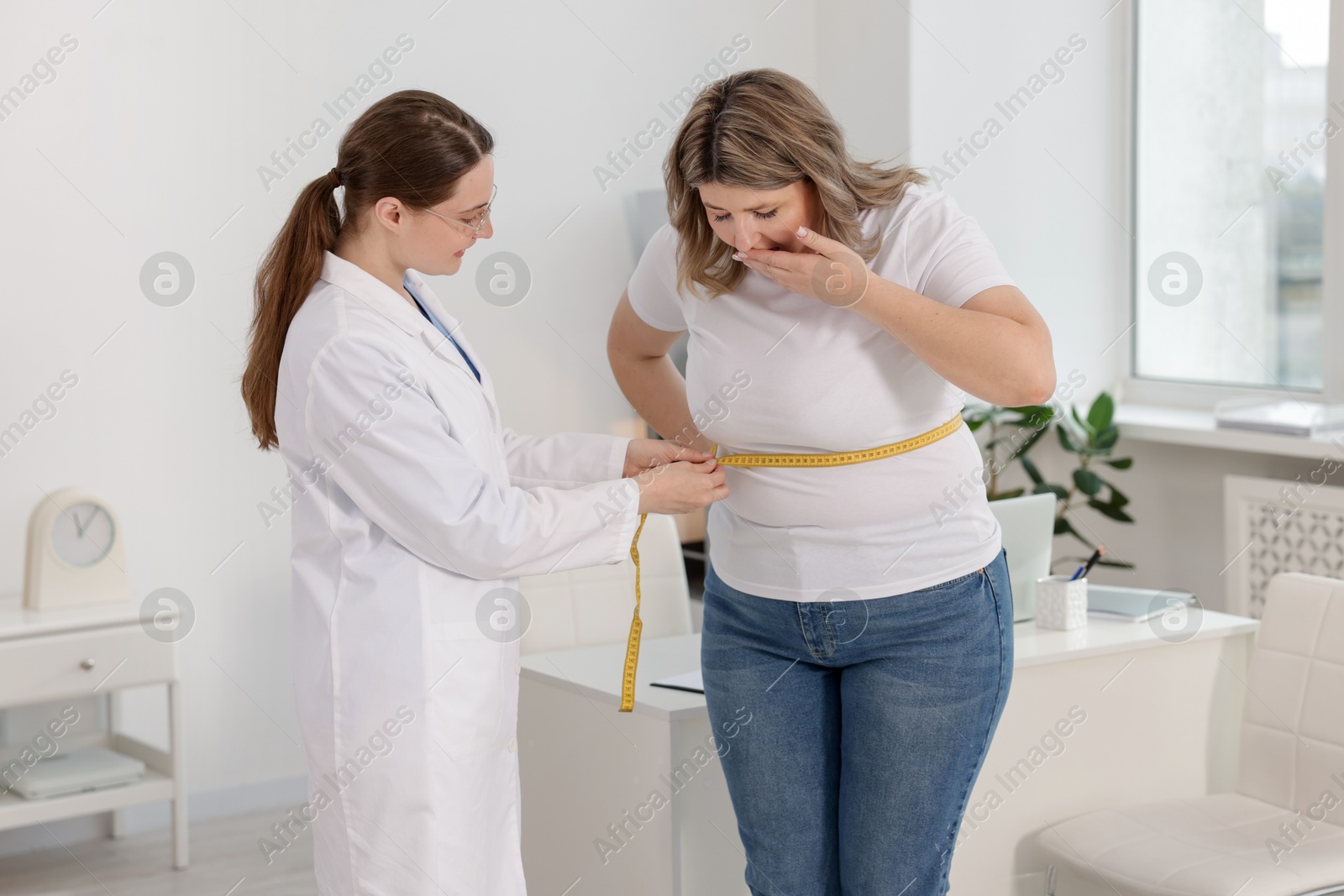 Weight loss. Nutritionist measuring shocked overweight woman's waist with tape in clinic Photo of Weight loss. Nutritionist measuring shocked overweight woman's waist with tape in clinic