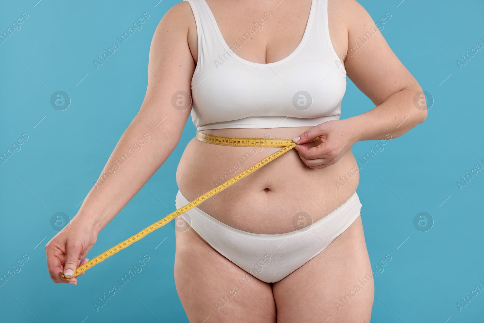 Weight loss. Plus size woman measuring waist with tape on light blue background, closeup Photo of Weight loss. Plus size woman measuring waist with tape on light blue background, closeup