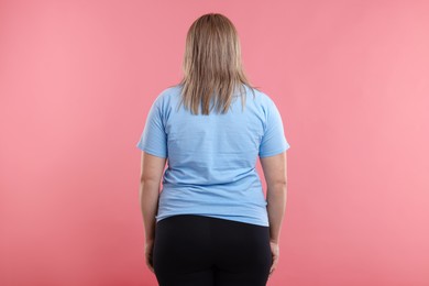 Photo of Weight loss. Plus size woman on pink background, back view