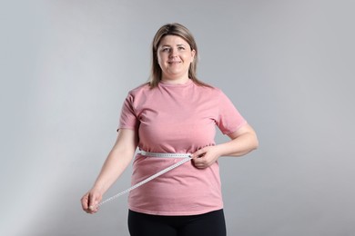 Photo of Weight loss. Plus size woman measuring waist with tape on gray background