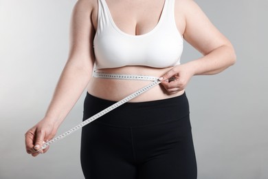 Photo of Weight loss. Plus size woman measuring waist with tape on gray background, closeup