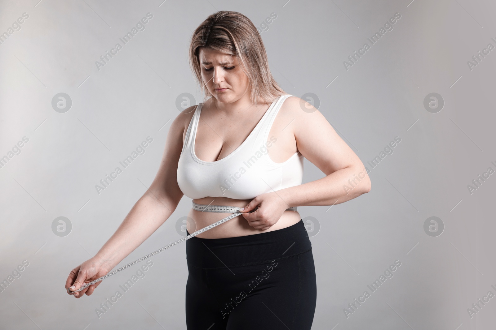 Photo of Weight loss. Plus size woman measuring waist with tape on gray background