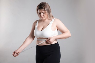 Photo of Weight loss. Plus size woman measuring waist with tape on gray background