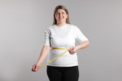 Photo of Weight loss. Plus size woman measuring waist with tape on gray background