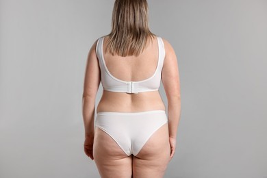 Photo of Weight loss. Plus size woman in underwear on gray background, back view