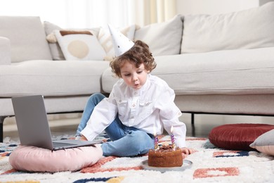 Photo of Birthday celebration. Little boy with cake having video call via laptop at home