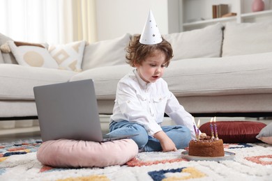 Photo of Birthday celebration. Little boy with cake having video call via laptop at home