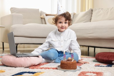 Photo of Birthday celebration. Little boy with cake having video call via laptop at home
