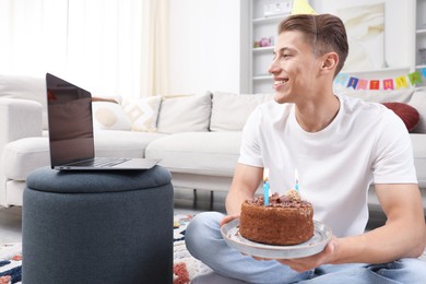 Photo of Man with cake celebrating his birthday and having video call via laptop at home