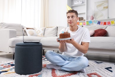 Photo of Birthday celebration. Man with cake making wish while having video call via laptop at home