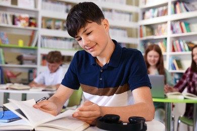 Photo of Student with books studying at table in library