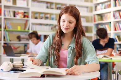 Photo of Student with books studying at table in library