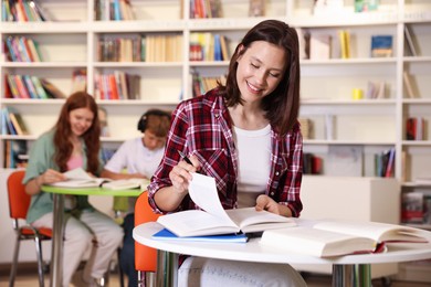 Photo of Student with books studying at table in library